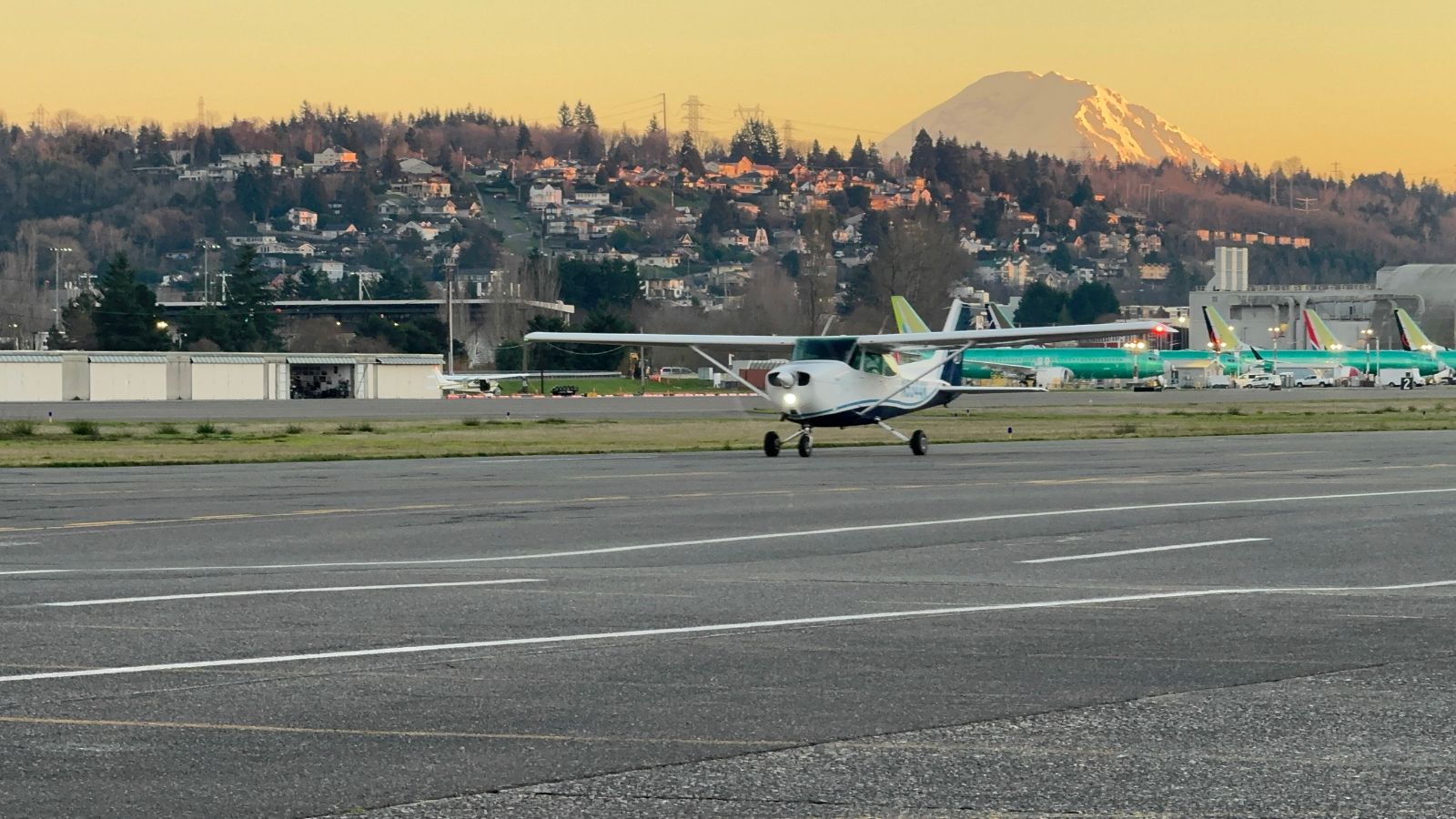 A Cessna taxiing at Renton at sunset, with Mount Rainier and a row of 737s behind it.