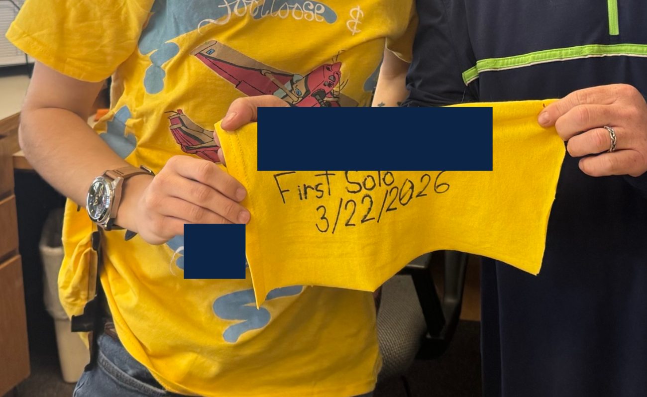 Hands holding a yellow first-solo cloth dated 3/22/2026. The name on the cloth is covered.